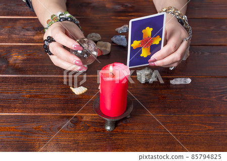 A fortune teller holds a magic ball and a Tarot card with a heart.The Gypsy lays out Tarot cards and guesses for the future.Magical sessions with the cards.Clairvoyance A fortune teller holds a magic ball and a Tarot card with a heart.The Gypsy lays out Tarot cards and guesses for the future.Magical sessions with the cards.Clairvoyance 85794825