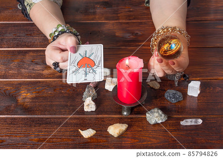 A fortune teller holds a magic ball and a Tarot card with a heart.The Gypsy lays out Tarot cards and guesses for the future.Magical sessions with the cards.Clairvoyance A fortune teller holds a magic ball and a Tarot card with a heart.The Gypsy lays out Tarot cards and guesses for the future.Magical sessions with the cards.Clairvoyance 85794826