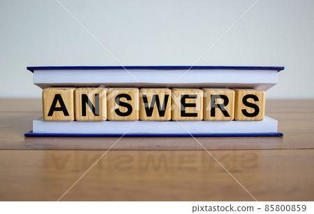 Concept word 'answers' on wooden cubes between pages of a book on a beautiful wooden table. White background. Business concept. 85800859