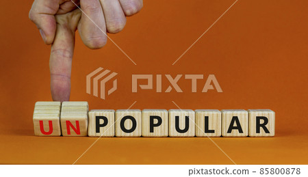 Popular or unpopular symbol. Businessman turns wooden cubes and changes the word unpopular to popular. Beautiful orange table, orange background. Popular or unpopular and business concept. Copy space. 85800878