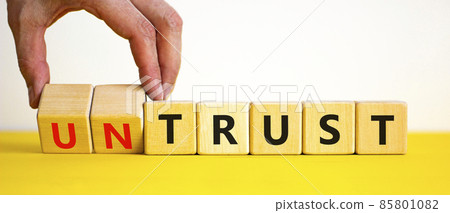 Untrust or trust symbol. Businessman turns wooden cubes, changes words 'untrust' to 'trust'. Beautiful yellow table, white background. Business and untrust or trust concept, copy space. Untrust or trust symbol. Businessman turns wooden cubes, changes words 'untrust' to 'trust'. Beautiful yellow table, white background. Business and untrust or trust concept, copy space. 85801082