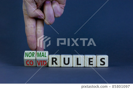Symbol of covid-19 or normal rules. Doctor turns wooden cubes and changes words 'covid rules' to 'normal rules'. Beautiful grey background, copy space. Medical, covid-19 or normal rules concept. 85801097