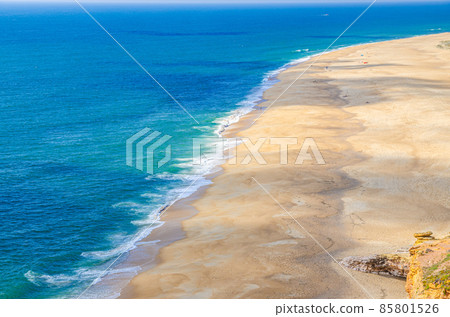 Top aerial panoramic view of sandy beach, waves of azure blue water of Atlantic Ocean and endless horizon near Nazare town Top aerial panoramic view of sandy beach, waves of azure blue water of Atlantic Ocean and endless horizon near Nazare town 85801526