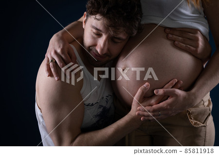 The husband closes his eyes and puts his ear to his wife's pregnancy belly. Hands on the stomach. Ninth month of pregnancy. Blessed state. 85811918