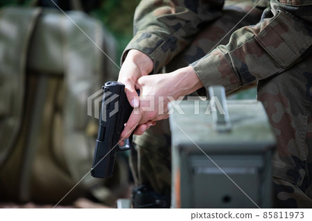 The lady soldier sits on a chair and holds a gun in her hands. The lady soldier sits on a chair and holds a gun in her hands. 85811973