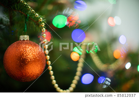 Gold orange Christmas tree bauble hangs on a Christmas tree at Christmas. Shiny Christmas tree lights in the background. 85812037