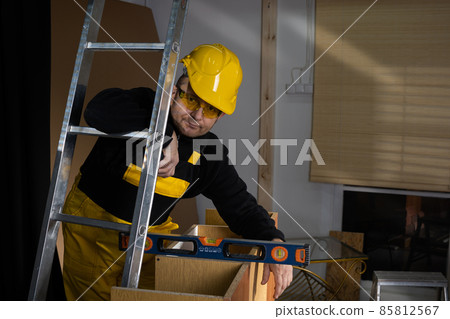 The builder checks with a spirit level that the cabinet is made correctly and without deviations. Construction worker wearing personal protective equipment. 85812567