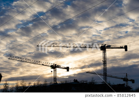 A tall construction crane against the setting sun. Machine for high-altitude lifting of building materials. 85812645
