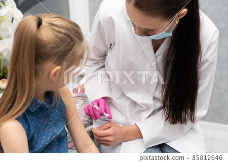 A nurse is getting ready to inject a little girl with a previously prepared vaccine. The young apprentice tries to talk to the child so that she is not afraid of the injection. A nurse is getting ready to inject a little girl with a previously prepared vaccine. The young apprentice tries to talk to the child so that she is not afraid of the injection. 85812646