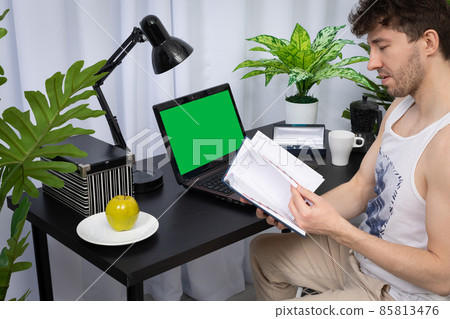 An employee quickly browses a book calendar to find the right information. A domain computer workstation among potted plants with bright lighting. Green screen of monitor ready to design. An employee quickly browses a book calendar to find the right information. A domain computer workstation among potted plants with bright lighting. Green screen of monitor ready to design. 85813476