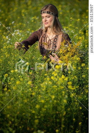 An herbalist checks her cultivated rapeseed fields. She holds a bouquet of herbs. An herbalist checks her cultivated rapeseed fields. She holds a bouquet of herbs. 85813697