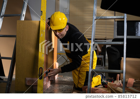 The manual worker checks with a spirit level that the decorative brick is correctly positioned. A construction worker dressed in personal protective equipment. 85813712