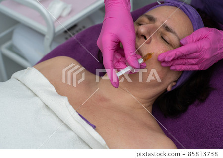 Applying the brightening serum with a syringe to reduce wrinkles and redness on the skin of the face 85813738
