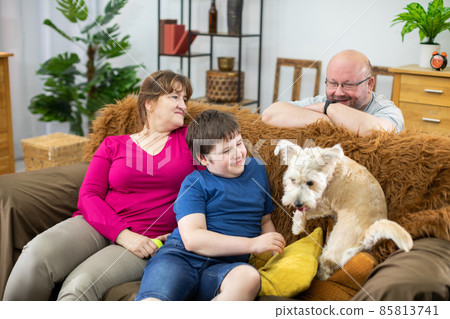 Wife and son are sitting on sofa and husband is playing with shaggy dog. Multiracial dog. Wife and son are sitting on sofa and husband is playing with shaggy dog. Multiracial dog. 85813741