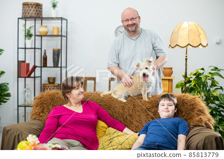 The father stands behind the sofa and strokes the shaggy dog the rest of the family watches all the fun. 85813779