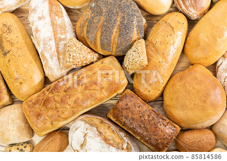 Many kinds of bread and buns randomly placed next to each other on a wooden countertop as decoration of a traditional bakery with a multi-generational experience. View from above. Many kinds of bread and buns randomly placed next to each other on a wooden countertop as decoration of a traditional bakery with a multi-generational experience. View from above. 85814586