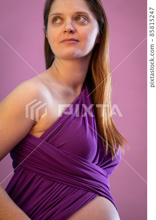 On a slightly pink background, there is a smiling young girl wearing a purple scarf in advanced pregnancy. 85815247