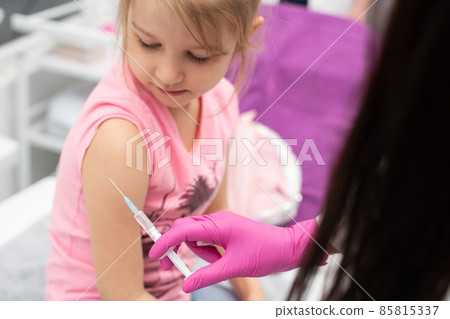 The doctor is giving a little girl an injection. The child stares in a choking bowl. Preventive vaccine for young children. The doctor is giving a little girl an injection. The child stares in a choking bowl. Preventive vaccine for young children. 85815337