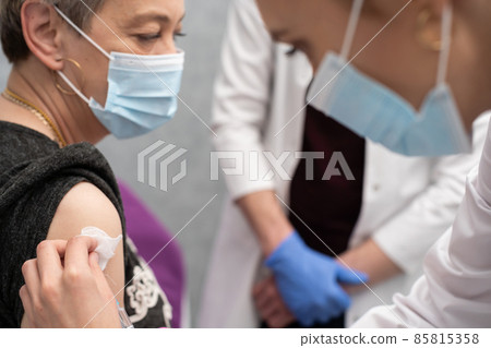 A nurse is making an vaccine to an elderly woman. The COVID vaccine19. A sterile doctor's office in a private clinic. A young medical intern looks at how to properly inject. 85815358