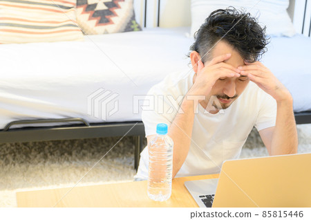 A middle-aged man holding his head in front of a computer and having a copy space on the left A middle-aged man holding his head in front of a computer and having a copy space on the left 85815446