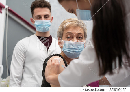 A nurse is making an vaccine to an elderly woman. The COVID vaccine19. A sterile doctor's office in a private clinic. A young medical intern looks at how to properly inject. 85816451