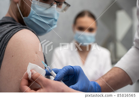 A nurse gives an injection to a patient with the COVID19 vaccine. A sterile doctor's office in a private clinic. A young medical intern looks at how to properly inject. 85816565