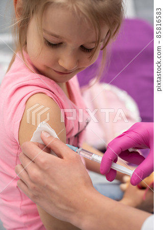 The doctor is giving a little girl an injection. The child stares in a choking bowl. Preventive vaccine for young children. 85816583