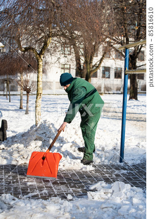 The landlord scrapes snow and ice with an orange cobblestone shovel 85816610