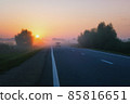 Car Drives On The Suburban Road On A Foggy Morning During Golden Sunrise 85816651