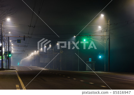 empty foggy night road with rows of lamp posts, green traffic light and pedestrian crossing empty foggy night road with rows of lamp posts, green traffic light and pedestrian crossing 85816947
