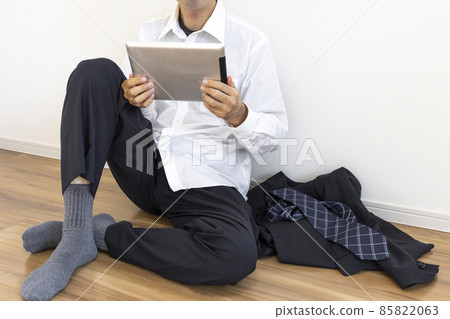 A man who takes off his suit, relaxes and uses a tablet device 85822063