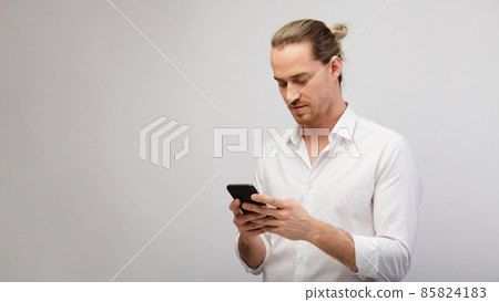 Young blonde bearded man texting message on smart phone over a white studio background with copy space Young blonde bearded man texting message on smart phone over a white studio background with copy space 85824183