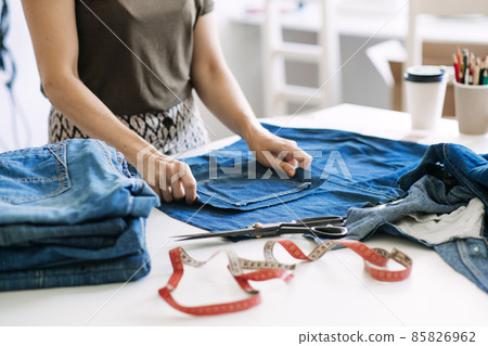 Circular economy. Sustainable fashion. Reuse, repair, upcycle. Denim upcycling ideas, repair and using old jeans. Woman seamstress repair old denim jeans in Sewing studio. Circular economy. Sustainable fashion. Reuse, repair, upcycle. Denim upcycling ideas, repair and using old jeans. Woman seamstress repair old denim jeans in Sewing studio. 85826962