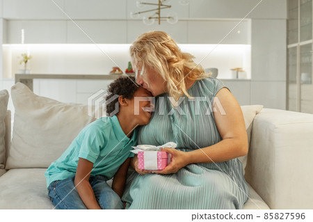 Mother kisses and hugging her son with gift box at home. Mothers day concept 85827596