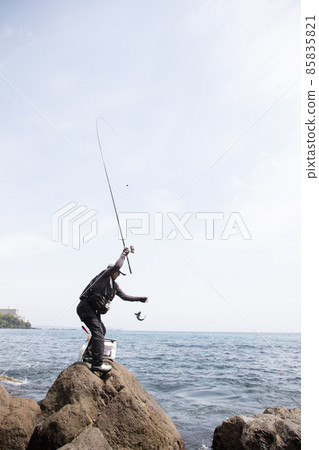 A man who caught a fish by rocky shore fishing 85835821