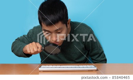 Young man using computer keyboard with magnifying glass to searching information. isolated on blue background 85840465