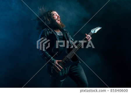 Expressive rock male guitarist with long hair and beard plays on the smoke background. Studio shot Expressive rock male guitarist with long hair and beard plays on the smoke background. Studio shot 85840600