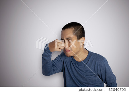 Portrait of young man pinching nose on his face due to bad smell isolated on gray background 85840703