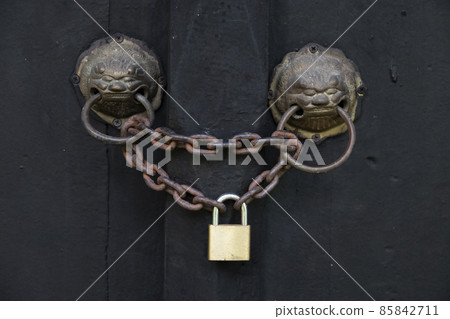 Ancient door with a lion head knocker are locked by an old chain and padlock. Ancient door with a lion head knocker are locked by an old chain and padlock. 85842711