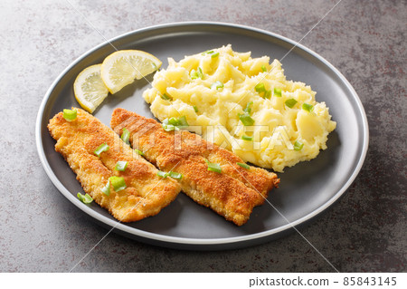 Sea fish fillet fried in breadcrumbs and a side dish of mashed potatoes close-up in a plate. horizontal 85843145