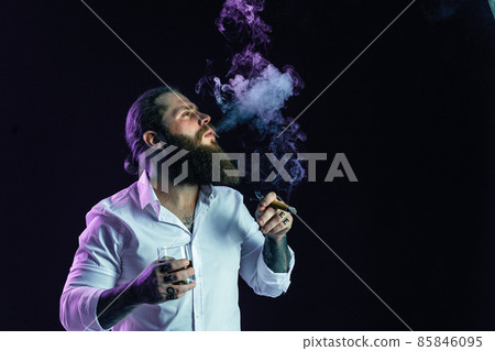 hipster bearded man in white shirt blowing smoke holds glass of whiskey and cigar. Studio shot hipster bearded man in white shirt blowing smoke holds glass of whiskey and cigar. Studio shot 85846095
