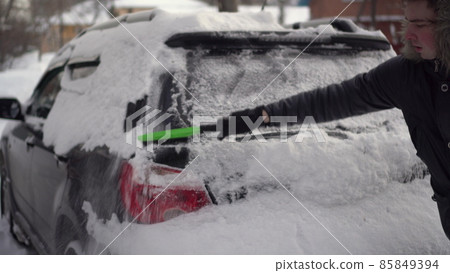 A man cleans the back of his car from snow with a brush close-up. The car was covered in snow. Weather disaster. A man cleans the back of his car from snow with a brush close-up. The car was covered in snow. Weather disaster. 85849394