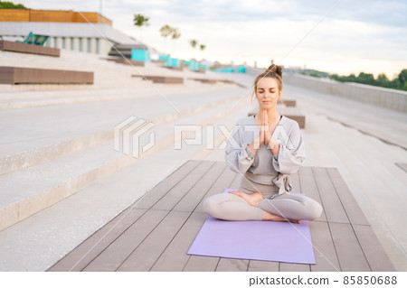Portrait of attractive Caucasian young woman practicing yoga performing namaste pose with closed eyes outside in city park. Portrait of attractive Caucasian young woman practicing yoga performing namaste pose with closed eyes outside in city park. 85850688
