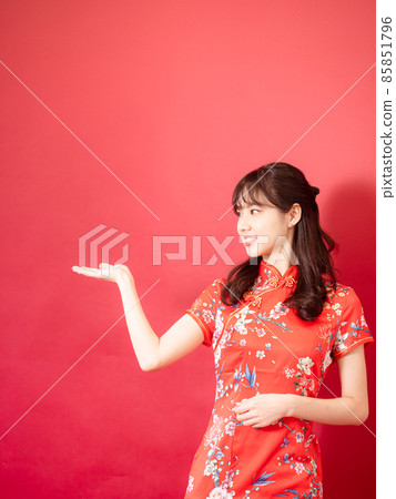 A beautiful woman with a cheongsam, a red-colored background with a smile on her face. 85851796