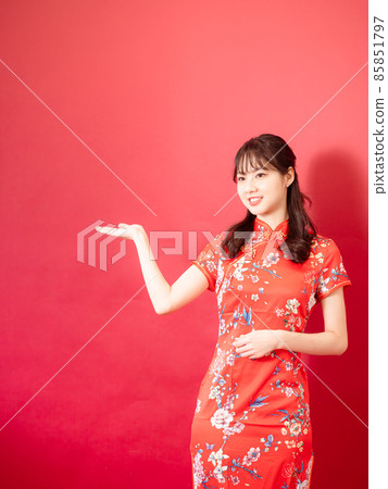 A beautiful woman with a cheongsam, a red-colored background with a smile on her face. 85851797