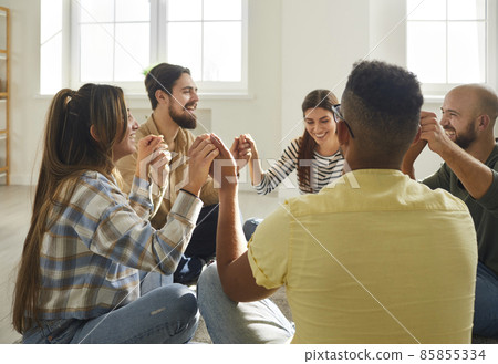 Diverse group of happy young people having fun time together. Cheerful mixed race friends sitting in circle on floor at home, holding hands and laughing at funny joke. Community and friendship concept Diverse group of happy young people having fun time together. Cheerful mixed race friends sitting in circle on floor at home, holding hands and laughing at funny joke. Community and friendship concept 85855334