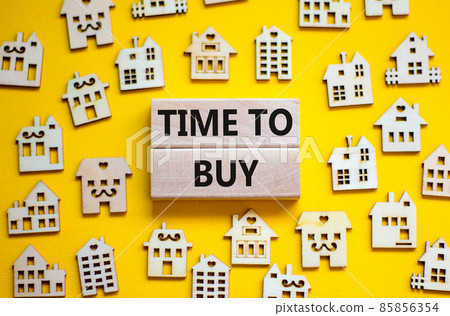 Time to buy house symbol. Concept words 'Time to buy' on wooden blocks near miniature houses. Beautiful yellow background, copy space. Business and time to buy house concept. 85856354
