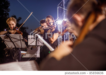Violin players playing in orchestra at night outdoor concert 85856636