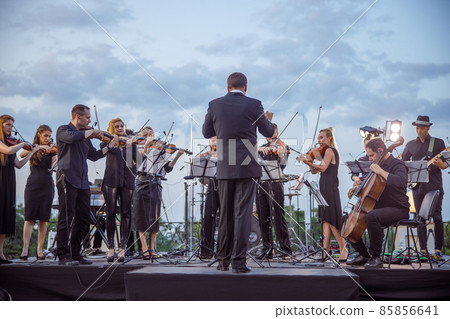 Orchestra playing classic instrumental music under cloudy sky 85856641