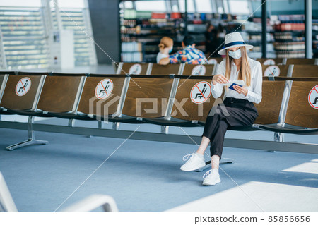 Young student college girl sitting at airport terminal wear medical mask feeling happy with safety travel bubble plan after covid pandemic and waiting for flight in fit to fly in concept. Young student college girl sitting at airport terminal wear medical mask feeling happy with safety travel bubble plan after covid pandemic and waiting for flight in fit to fly in concept. 85856656